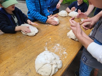 Kinder und Erwachsene stehen an einem Tisch und formen Brotlaibe aus einem Stück Teig.