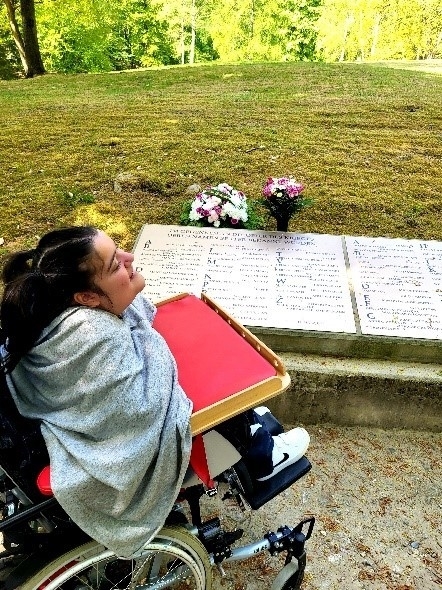 ein Mädchen im Rollstuhl vor einem Grabstein