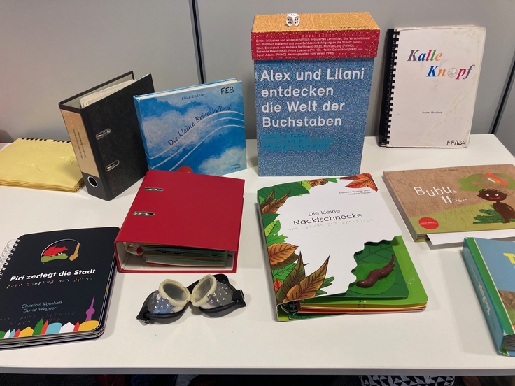 Das Bild zeigt einen Tisch mit verschiedenen Fühlbüchern für Kinder sowie einer Simulationsbrille.