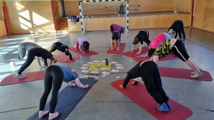 Ein paar Schüler:innen machen in einer Sporthalle Dehnübungen.