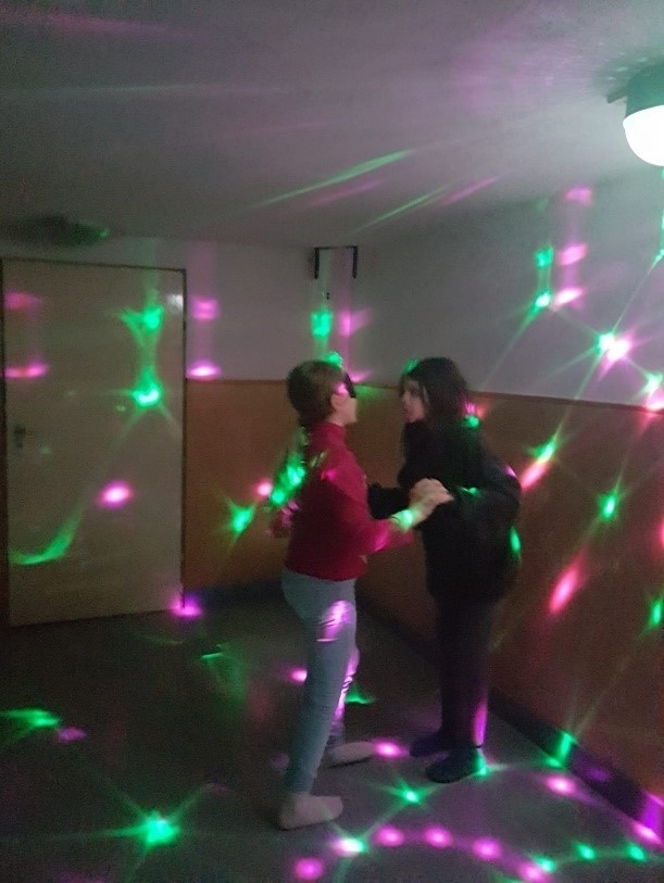 Zwei Schülerinnen tanzen in einer Disco mit bunten flackernden Licht.