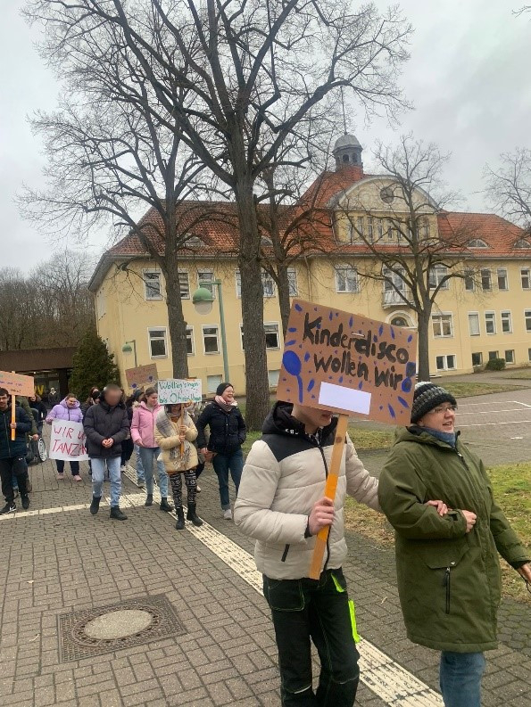 Mehrere Schüler:innen gehen über das Schulgelände und demonstrieren für eine Kinder-Disco.