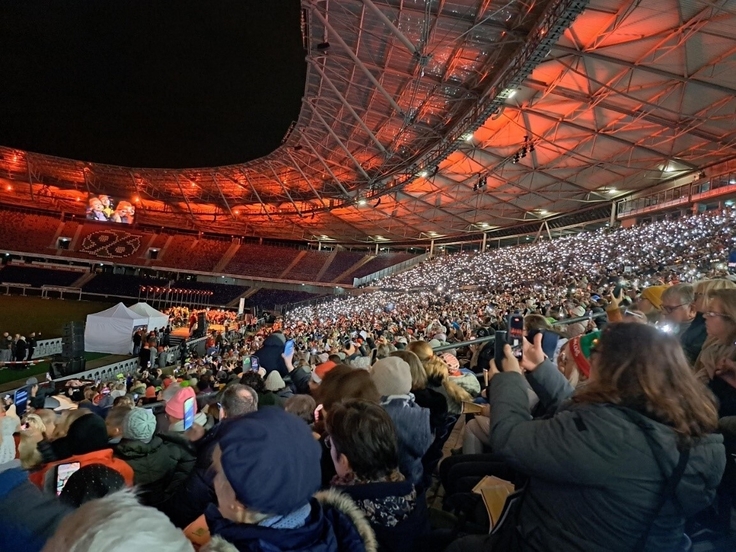 Viele Menschen sitzen auf der Tribüne der Heinz-von-Heiden Arena mit Handykameras in der Hand und singen Weihnachtslieder