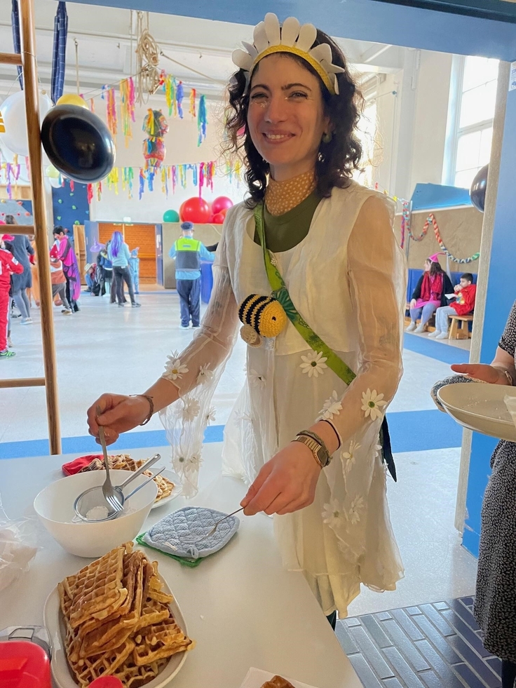 Frau Khan, als Schneeglöckchen verkleidet, bestreut Waffeln mit Puderzucker