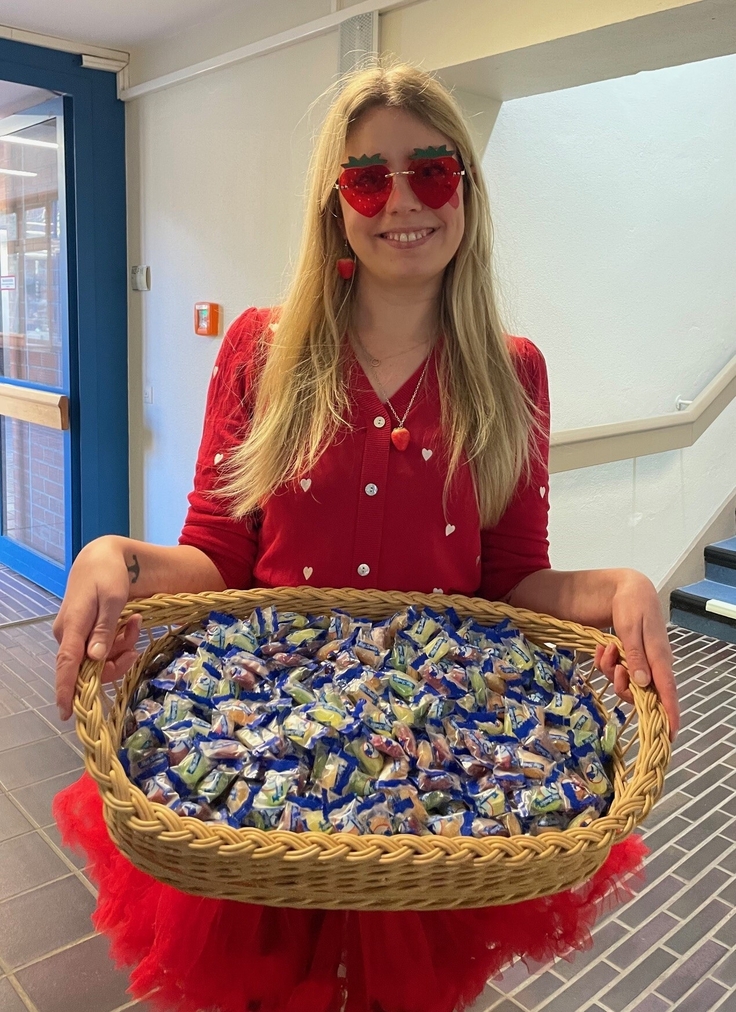 Frau Musäus, als Erdbeere verkleidet, hält in ihren Armen einen großen Korb voller Bonbons.