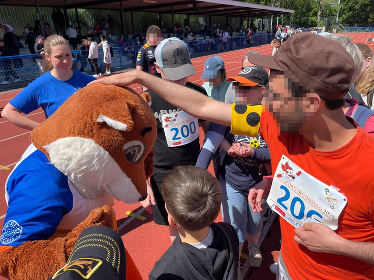 Mehrere Schülerinnen und Schüler begrüßen das Maskottchen Sporty.