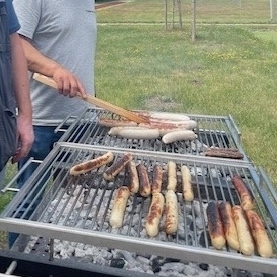 Zwei fleißige Kollegen stehen am Grill und kümmern sich um die Würstchen