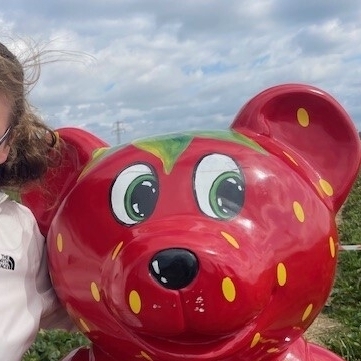 Eine weitere Schülerin steht bei dem Erdbär. Dieser ist eine große Bärfigur, die rot mit gelben Punkten angemalt ist und aussieht wie eine Erdbeere.