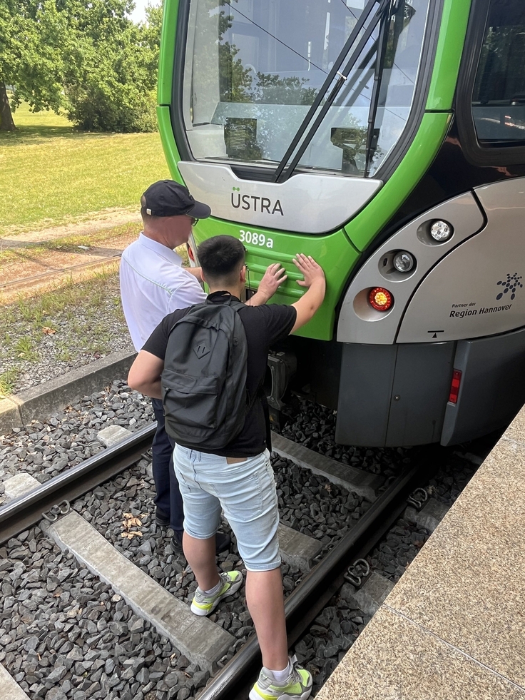 Ein Schüler steht im Gleisbett und erkundet die Vorderseite der neuen Bahn. Ein Mitarbeiter der Üstra erklärt ihm wofür die einzelnen Teil sind
