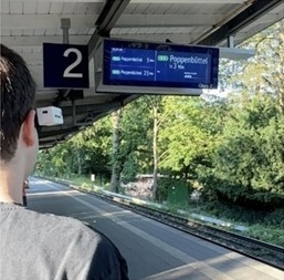 Ein blinder Jugendlicher steht draußen auf einem Bahnhof, er trägt den Prototypen.