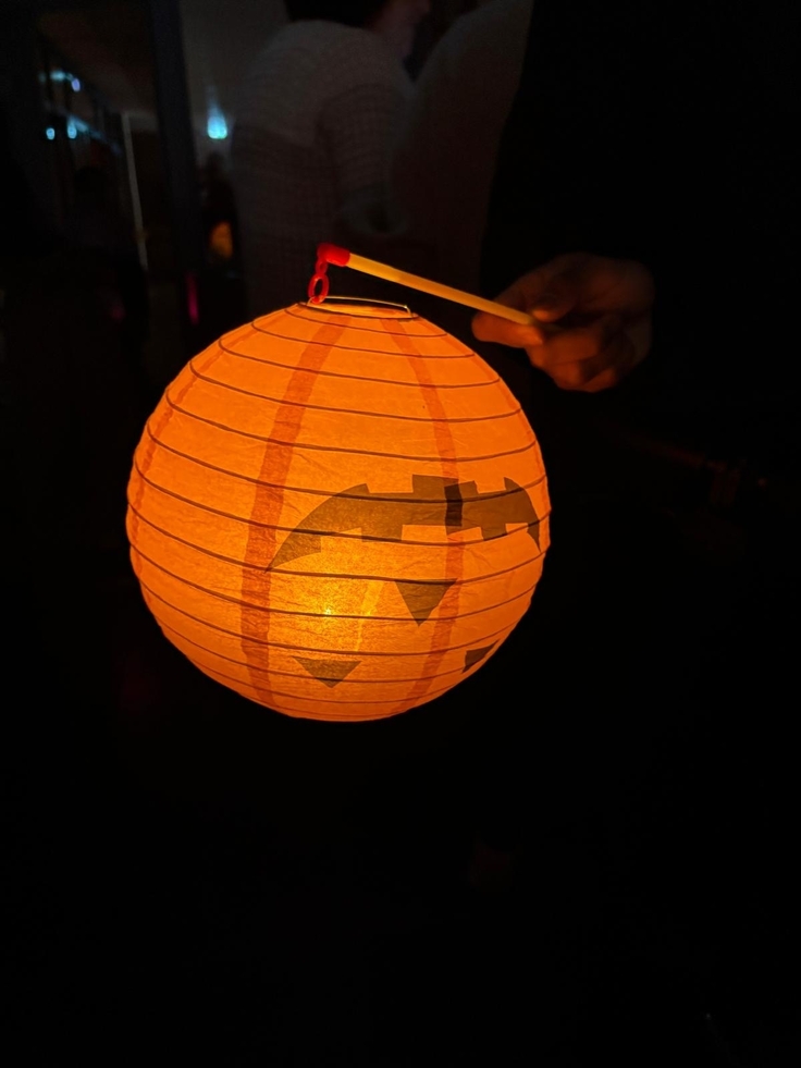 Orangene, runde Laterne mit einem Halloweengesicht, in der Hand eines Kindes. Das Gesicht auf der Laterne steht auf dem Kopf.