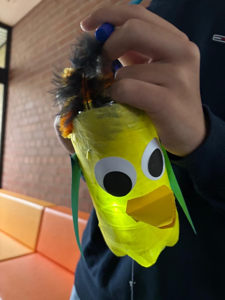 Aus einer Plastikflasche gebastelte grüne Vogellaterne, in der Hand eine Kindes.