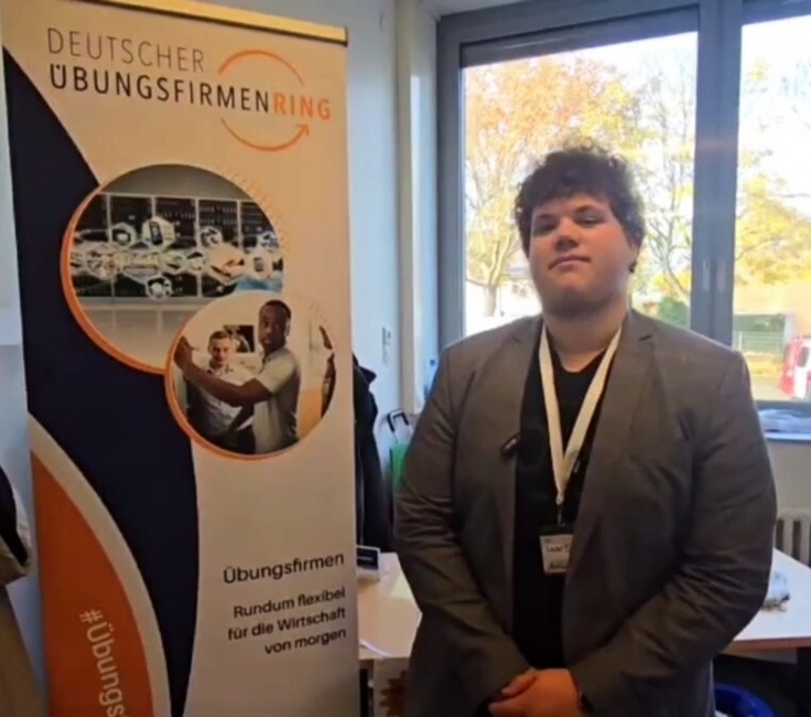 Ein Auszubildender steht vor einem Aufsteller der Übungsfirmenmesse.