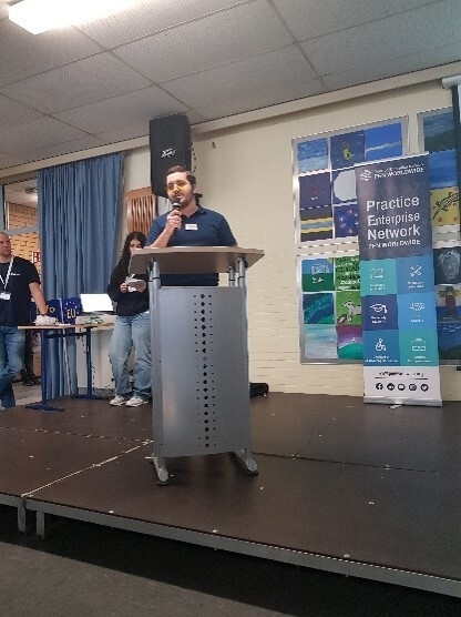 Ein Auszubildender steht an einem Pult und stellt die Firma LaserTec beim Pitch vor.