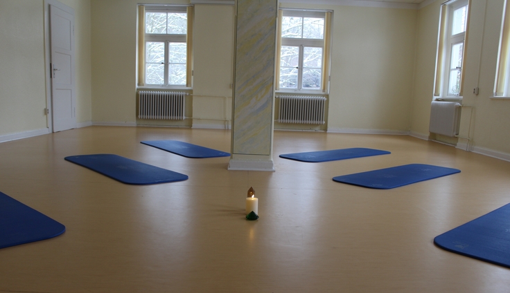 Ein Raum in dem mehrere Yogamatten auf dem Fußboden liegen.