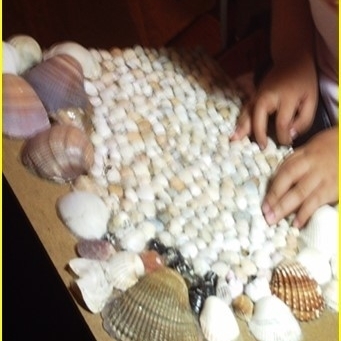 Ein Kind tastet ein aus Muscheln verschiedener Größe hergestelltes Reliefbild ab