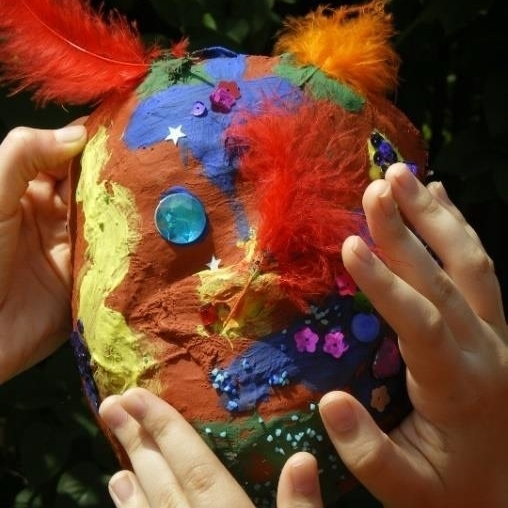 Drei Hände ertasten einen farbig und mit Material gestalteten Pappmaché-Ballon.