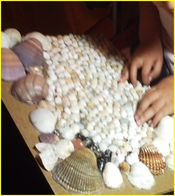 Ein Kind tastet ein aus Muscheln verschiedener Größe hergestelltes Reliefbild ab.