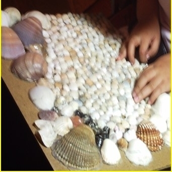 Ein Kind tastet ein aus Muscheln verschiedener Größe hergestelltes Reliefbild ab.