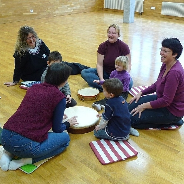 Eltern und Kinder sitzen im Kreis und musizieren mit Trommeln.