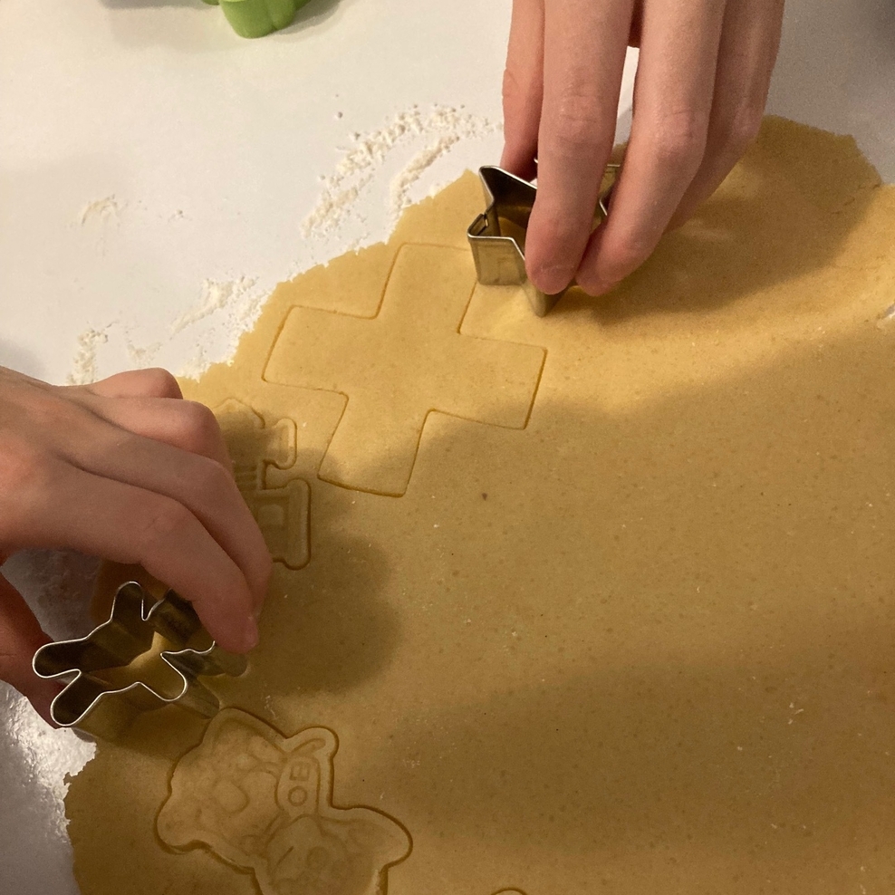 Zwei Kinderhände stechen mit Ausstechern aus einer ausgerollten Masse verschiedene Formen aus.