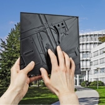 Jemand hält eine taktile Karte in den Händen und steht vor einem großen Gebäude.