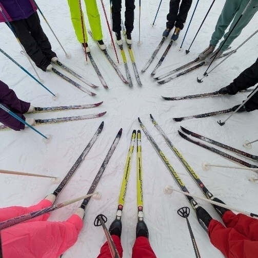 Mehrere Personen stehen mit Skiern in einem Kreis und jemand hat ein Foto von oben, von den Skiern gemacht.