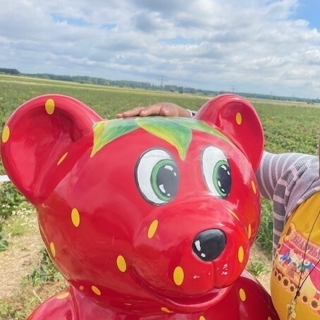 Eine Schülerin steht bei dem Erdbär. Dieser ist eine große Bärfigur, die rot mit gelben Punkten angemalt ist und aussieht wie eine Erdbeere.