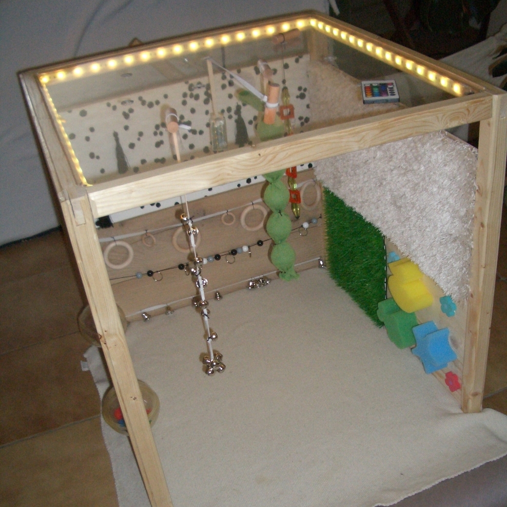 Das Bild zeigt den Nachbau eines „Kleinen Raums“ nach Lilli Nielsen: Drei Seitenwände aus Holz (links, rechts, hinten) sowie eine Plexiglasplatte (oben) bilden einen Würfel, der unten und vorne offen ist.