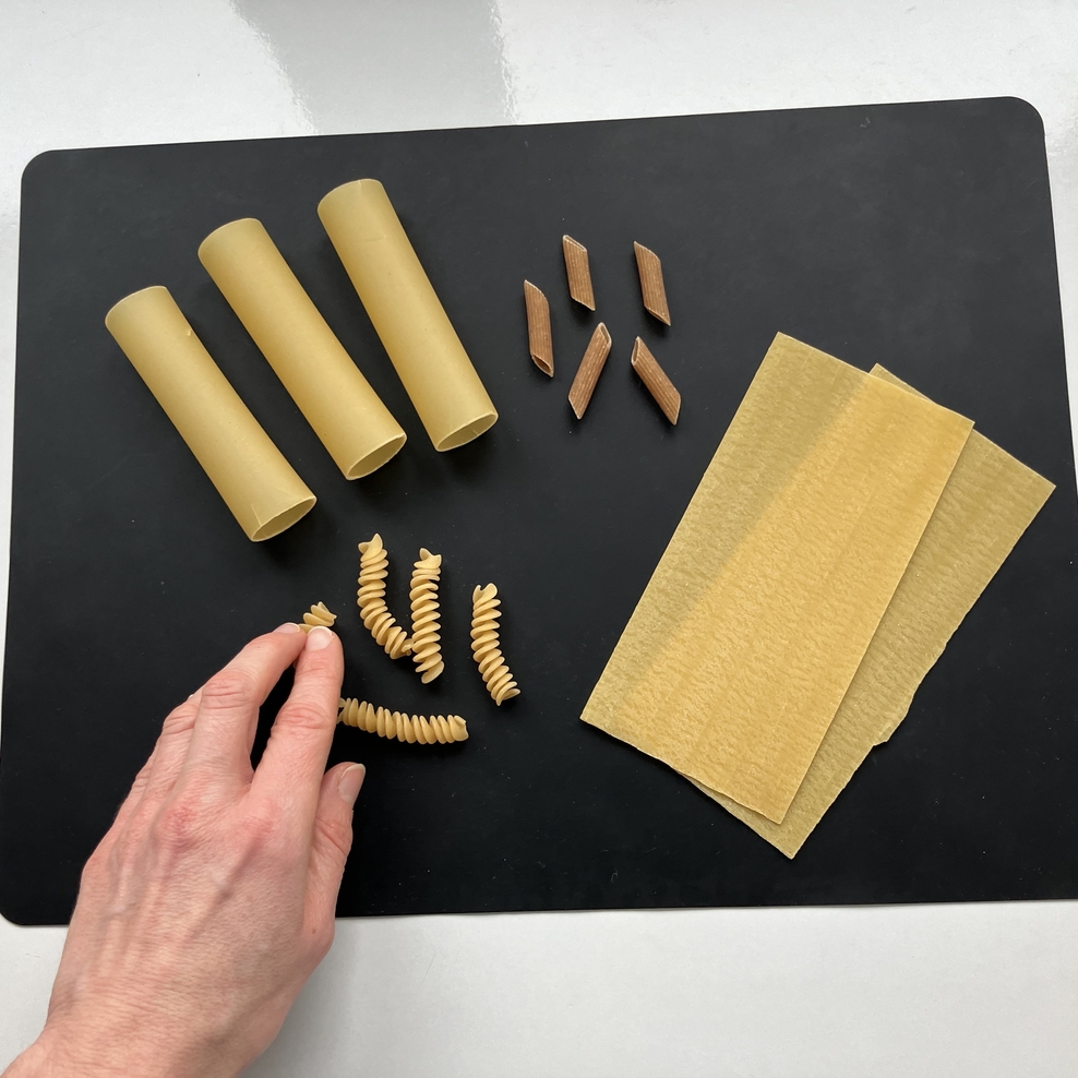 Die Welt wahrnehmen und begreifen. Auf einem Tisch liegen verschiedene rohe Nudelsorten und jemand fühlt die Nudeln.