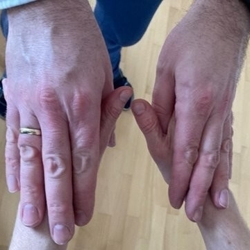 Zwei größere Hände liegen auf zwei kleineren Händen. Die oberen Hände fühlen die Bewegungen und taktilen Gebärden der unteren Hände.