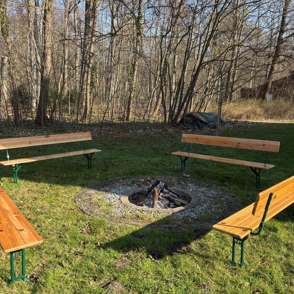 Vier Holzbänke stehen um das brennende Lagerfeuer herum.