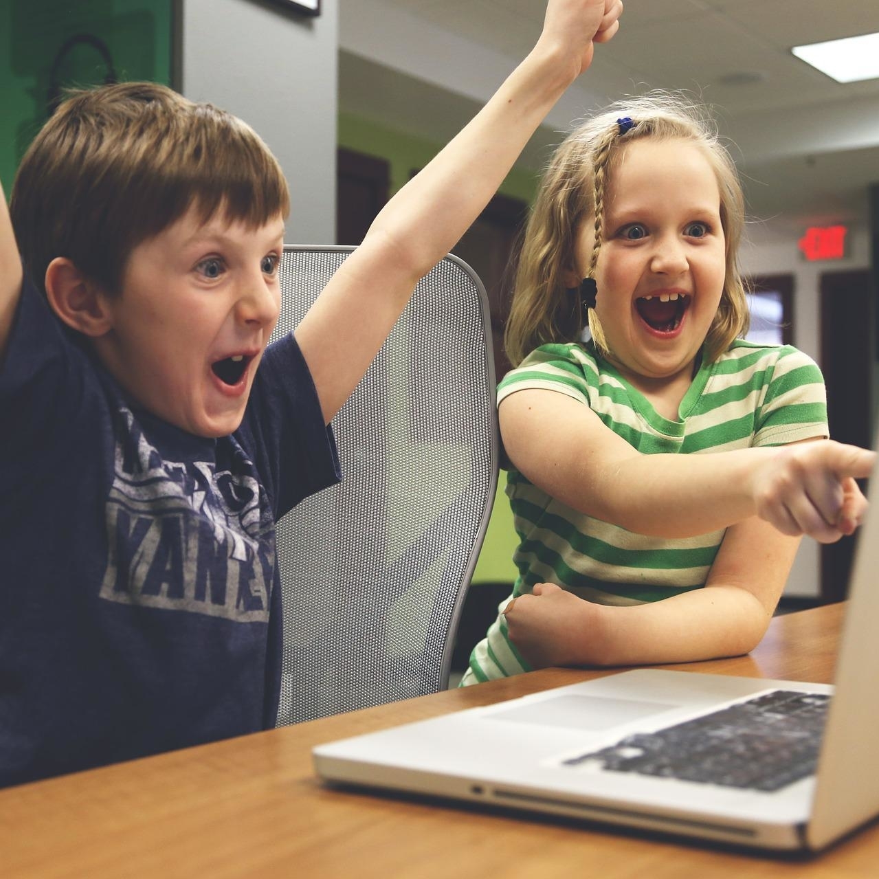 zwei Kinder vor einem Laptop, die jubeln und sich freuen